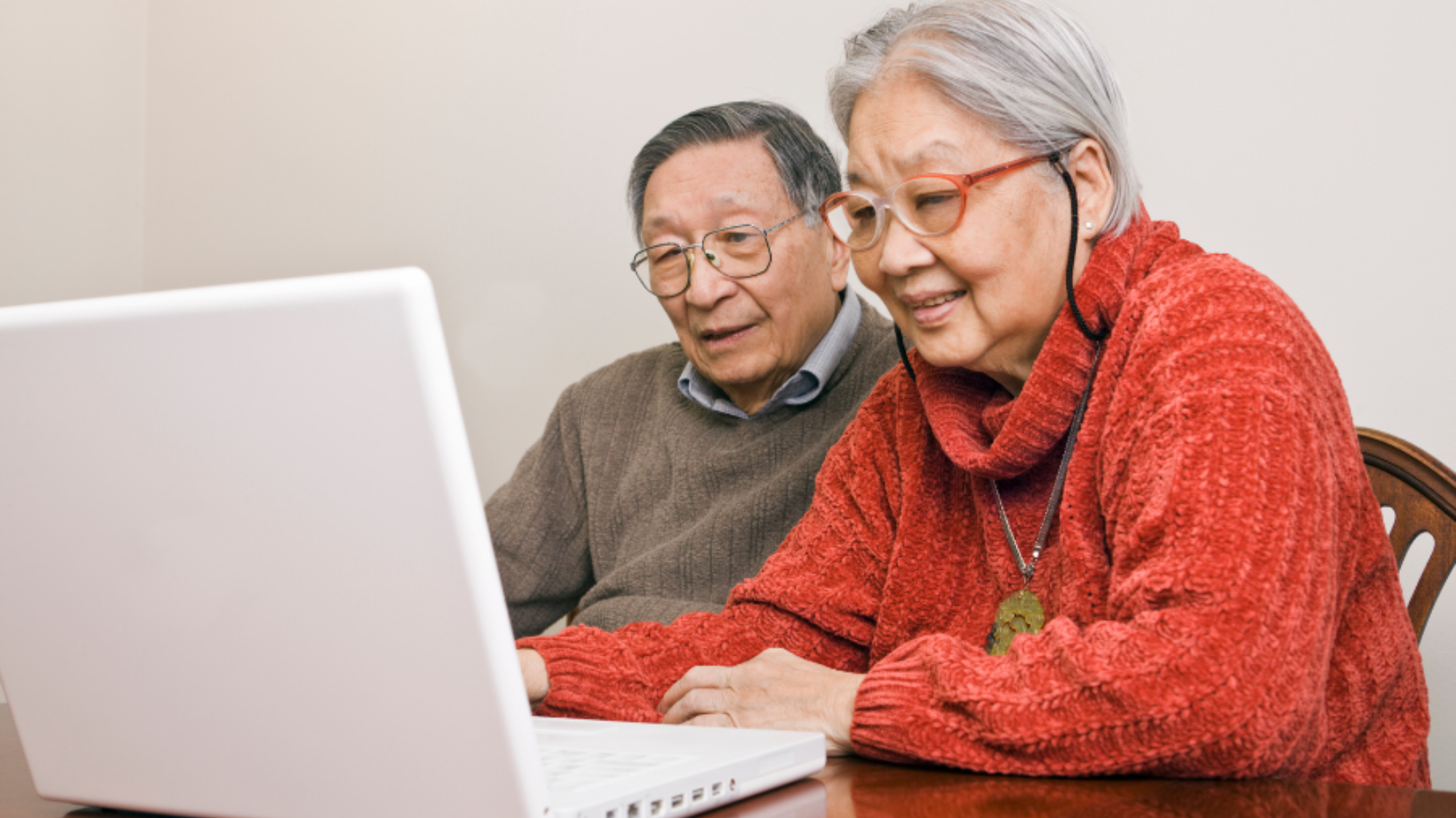 Two older adults attend a Felton Institute Tech Squad online class. They're siting at a table and looking at a laptop.